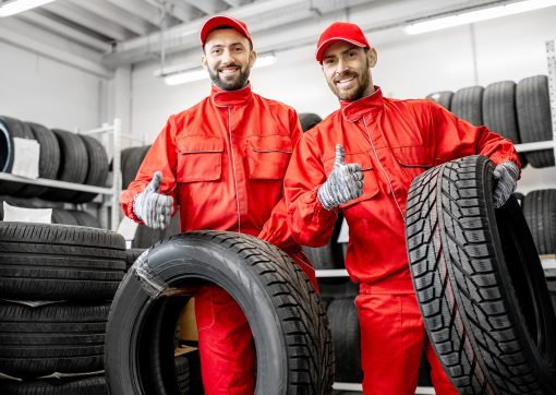 Portrait of a two workers in red uniform with car tires at the warehouse of the car service